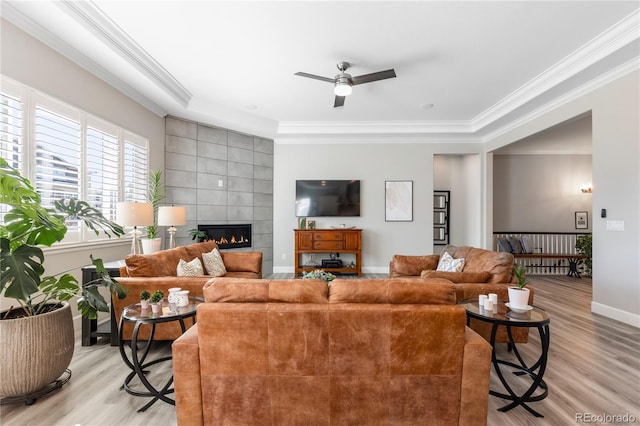 living room featuring baseboards, a tile fireplace, light wood-style flooring, and crown molding