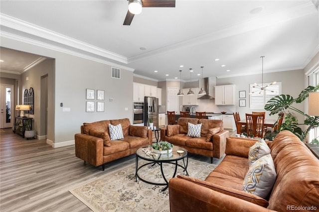 living room with light wood-style flooring, recessed lighting, ceiling fan with notable chandelier, visible vents, and baseboards