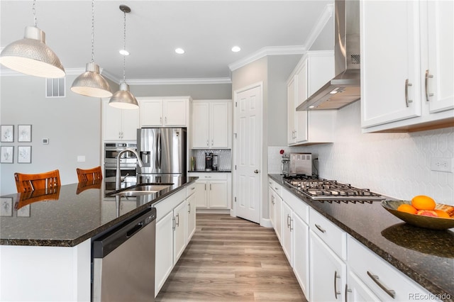 kitchen with crown molding, stainless steel appliances, white cabinets, a sink, and wall chimney range hood