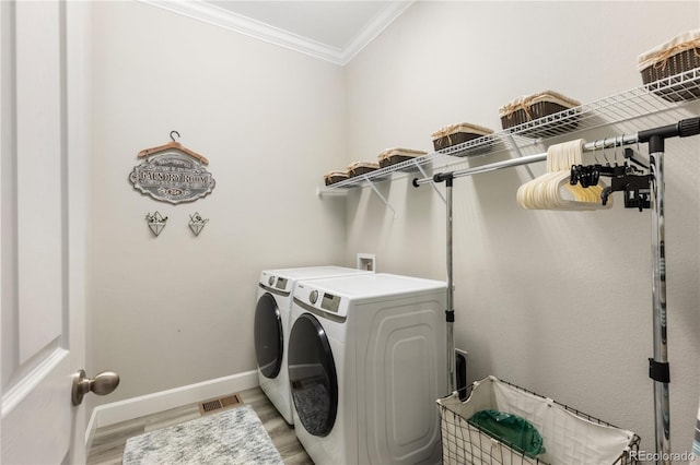 clothes washing area with laundry area, baseboards, crown molding, light wood-style floors, and washing machine and dryer