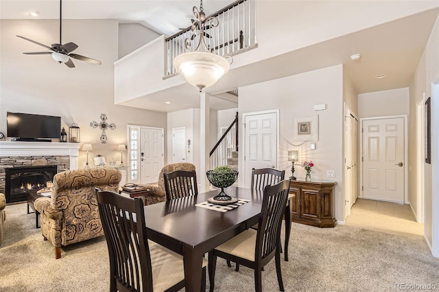 601 Clarendon Loop, Castle Pines, CO 80108 - dining area featuring light carpet, ceiling fan, a stone fireplace, stairway, and a towering ceiling