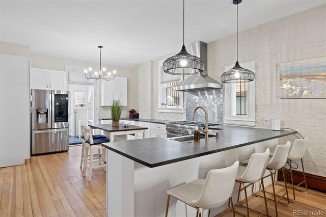 1554 N Pennsylvania St, Denver, CO 80203 - kitchen with white cabinetry, light wood-style floors, appliances with stainless steel finishes, wall chimney range hood, and dark countertops