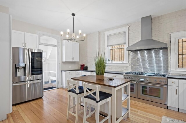 1554 N Pennsylvania St, Denver, CO 80203 - kitchen featuring white cabinets, light wood-style floors, appliances with stainless steel finishes, backsplash, and wall chimney exhaust hood