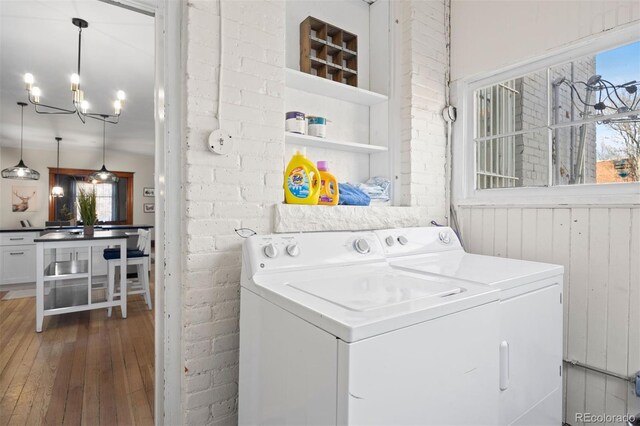 1554 N Pennsylvania St, Denver, CO 80203 - clothes washing area with washing machine and dryer, a notable chandelier, brick wall, laundry area, and hardwood / wood-style floors