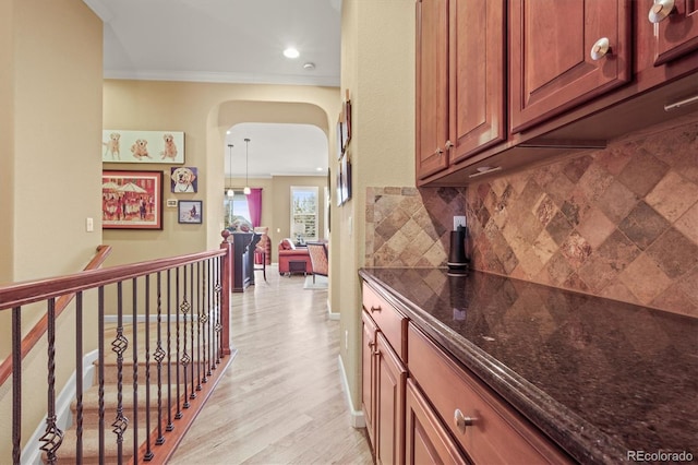 bar with dark stone countertops, decorative backsplash, hanging light fixtures, crown molding, and light wood-type flooring