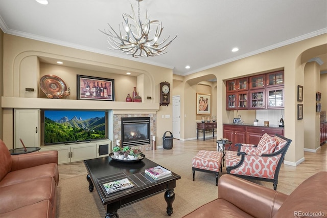 living room with a tiled fireplace, crown molding, a chandelier, and light hardwood / wood-style floors