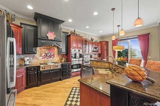 kitchen featuring sink, a center island with sink, light wood-type flooring, pendant lighting, and stainless steel appliances