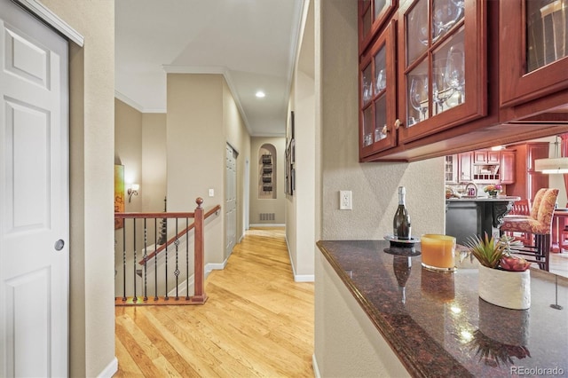 bar featuring crown molding, dishwasher, light wood-type flooring, and dark stone counters