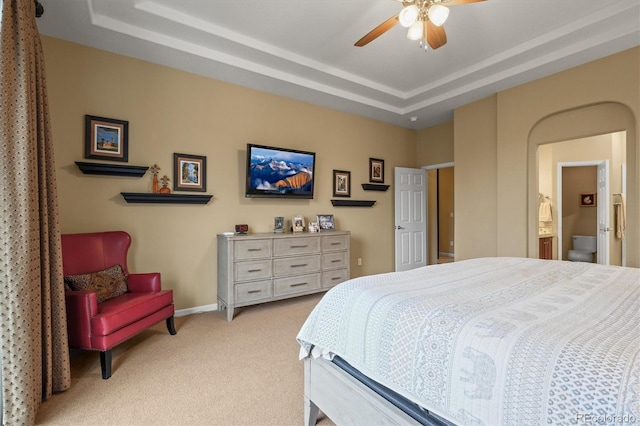 bedroom with ceiling fan, light colored carpet, ensuite bath, and a tray ceiling