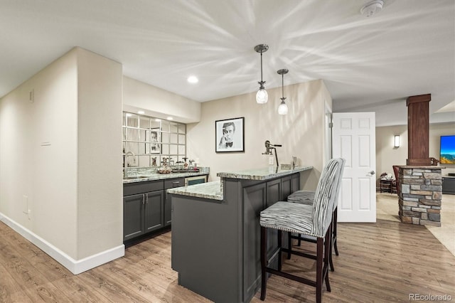 kitchen featuring a breakfast bar, sink, light stone counters, decorative light fixtures, and hardwood / wood-style floors