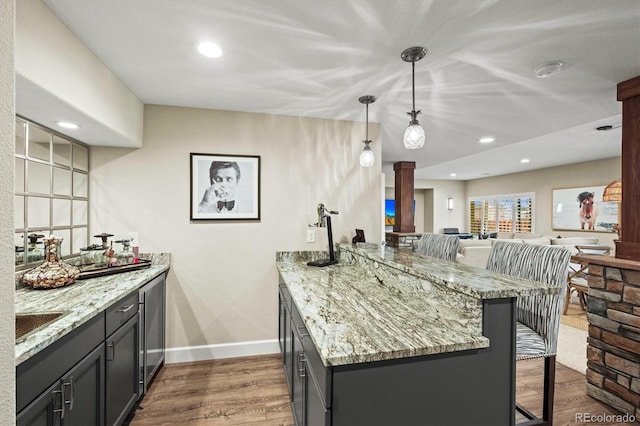 kitchen featuring ornate columns, dark hardwood / wood-style floors, decorative light fixtures, a kitchen bar, and light stone countertops