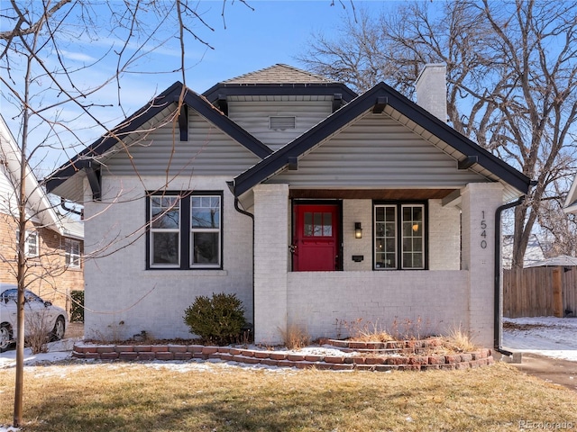 bungalow-style house featuring brick siding, a chimney, a porch, and a front lawn