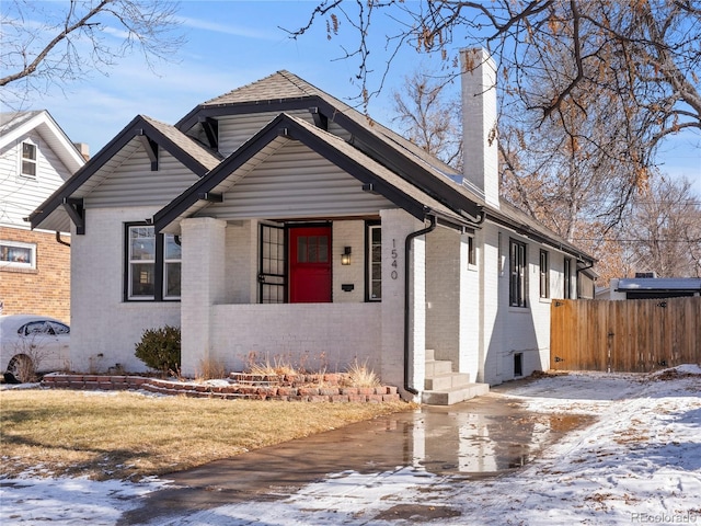 bungalow-style home featuring a chimney, fence, and brick siding