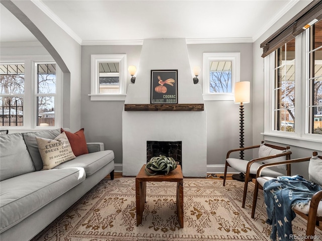 living area featuring a large fireplace, baseboards, arched walkways, light wood-style flooring, and ornamental molding