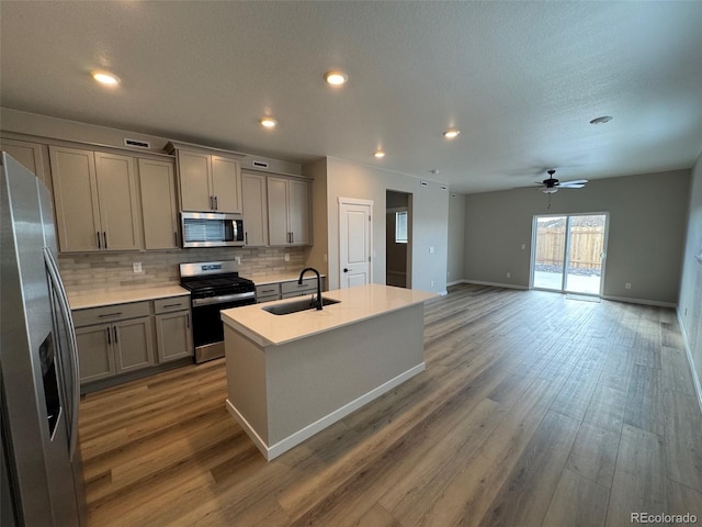 kitchen featuring a kitchen island with sink, stainless steel appliances, a sink, light countertops, and gray cabinets