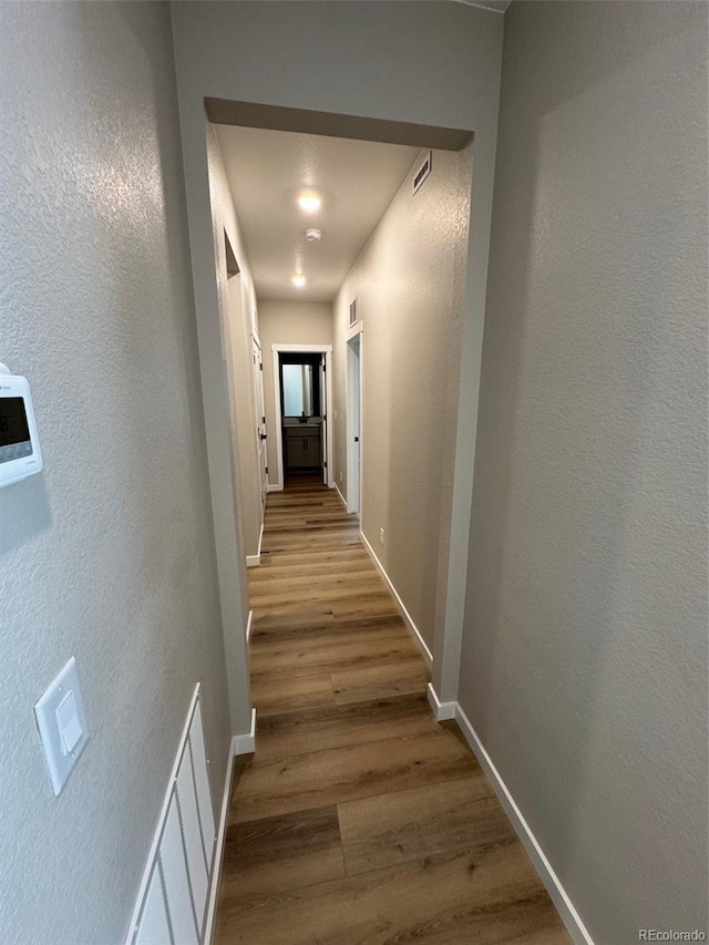 hallway featuring wood finished floors, baseboards, and a textured wall