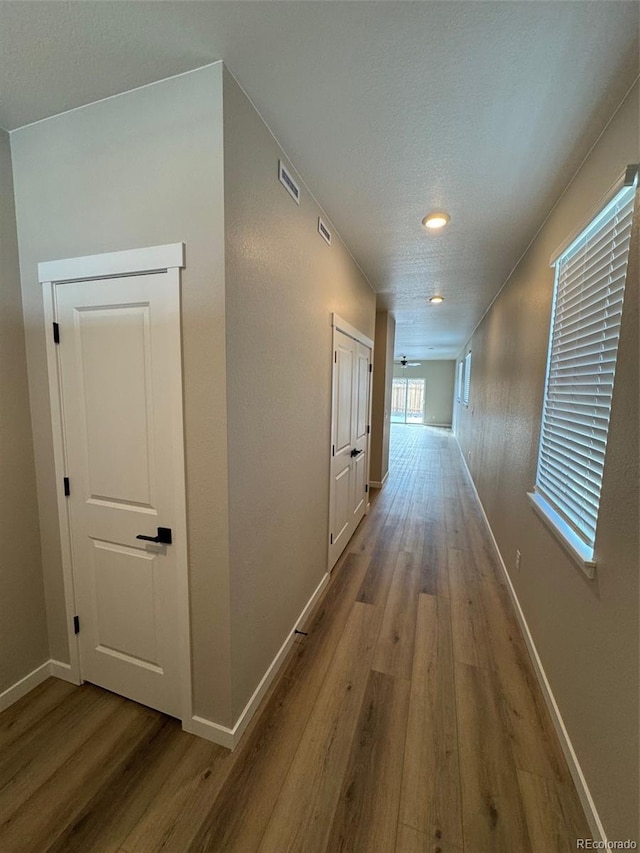 corridor with visible vents, a textured ceiling, baseboards, and wood finished floors