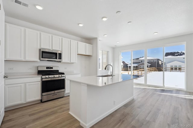 kitchen featuring sink, light hardwood / wood-style floors, stainless steel appliances, white cabinets, and a kitchen island with sink