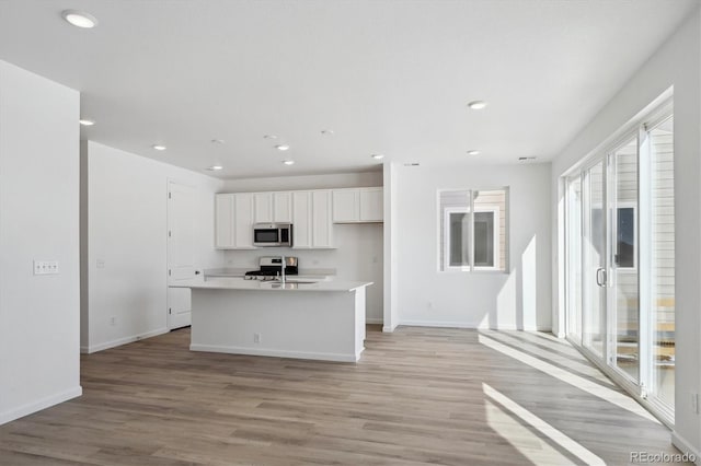 kitchen with white cabinets, an island with sink, appliances with stainless steel finishes, and light wood-type flooring