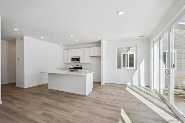 kitchen featuring appliances with stainless steel finishes, light hardwood / wood-style flooring, white cabinets, and a center island with sink