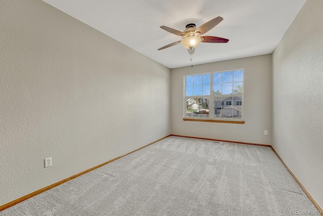 empty room with ceiling fan, a textured wall, baseboards, and light colored carpet