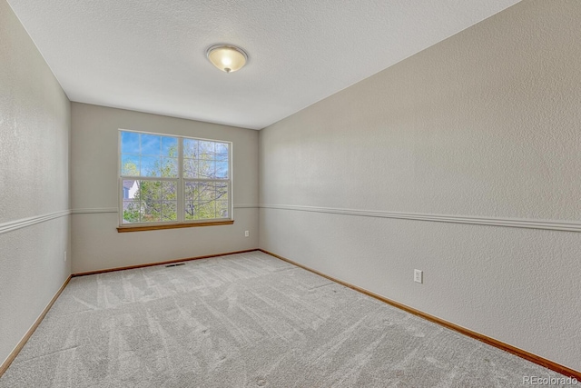 spare room featuring a textured wall, baseboards, and carpet floors