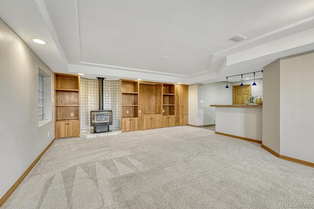 unfurnished living room with a wood stove, a raised ceiling, baseboards, and light carpet