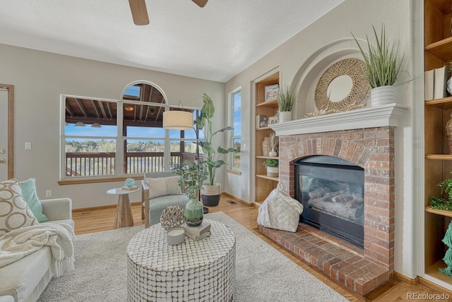 living room featuring a brick fireplace, ceiling fan, baseboards, and wood finished floors