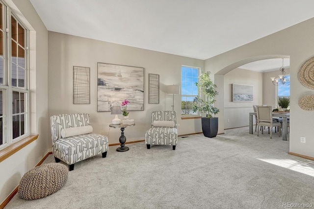 living area featuring arched walkways, baseboards, carpet floors, and a chandelier