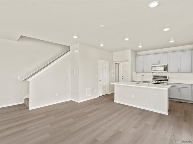 kitchen with appliances with stainless steel finishes, tasteful backsplash, sink, a kitchen island with sink, and light hardwood / wood-style floors