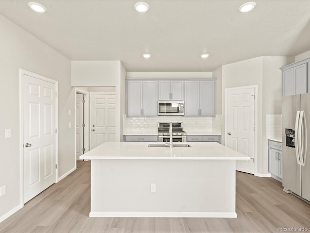 kitchen featuring a kitchen island with sink, decorative backsplash, gray cabinetry, and appliances with stainless steel finishes