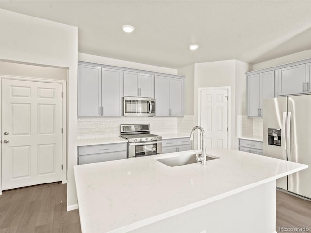 kitchen with sink, light hardwood / wood-style flooring, a kitchen island with sink, stainless steel appliances, and light stone countertops