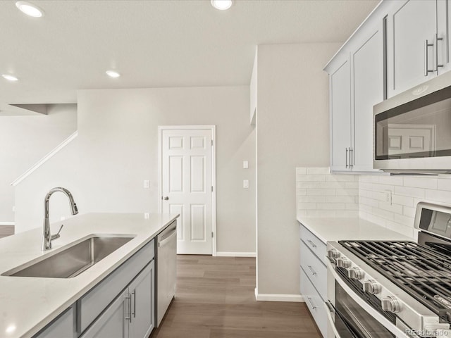 kitchen featuring stainless steel appliances, sink, wood-type flooring, and backsplash