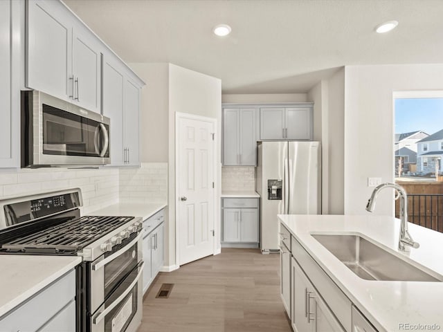 kitchen with sink, light hardwood / wood-style flooring, stainless steel appliances, light stone counters, and decorative backsplash