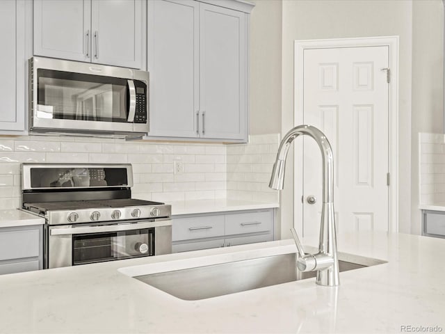 kitchen with tasteful backsplash, light stone countertops, stainless steel appliances, and sink