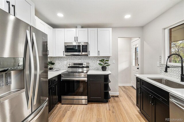 kitchen featuring stainless steel appliances, white cabinetry, light wood finished floors, a sink, and dark cabinetry