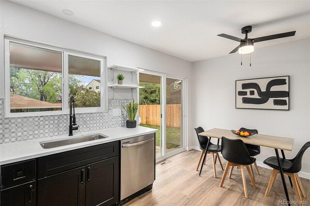 kitchen featuring dishwasher, a sink, dark cabinetry, light wood-type flooring, and plenty of natural light