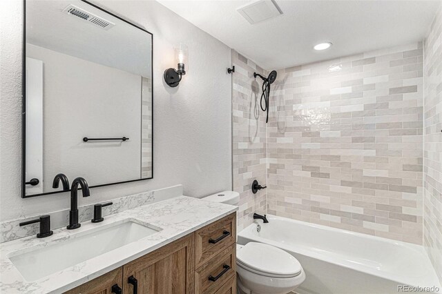 bathroom featuring toilet, shower / bath combination, vanity, and a textured wall