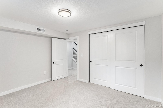 unfurnished bedroom with light colored carpet, baseboards, a textured ceiling, and a closet