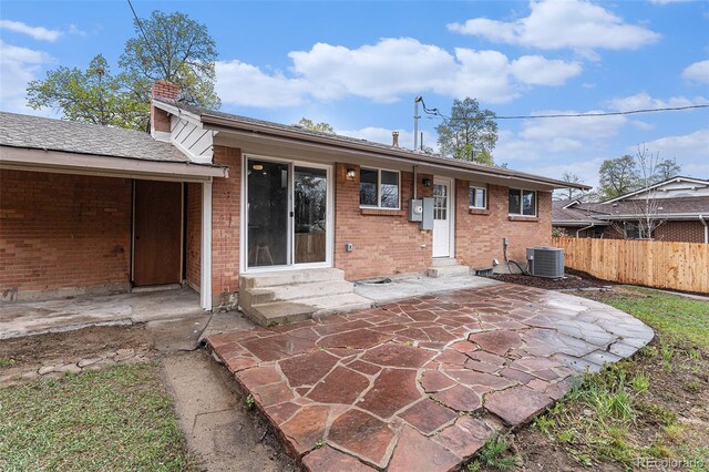 back of property featuring entry steps, fence, brick siding, a chimney, and a patio