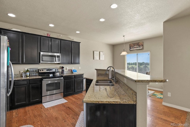 9233 Waters Edge Dr, Fountain, CO 80817 - kitchen featuring stainless steel appliances, a textured ceiling, light wood finished floors, dark cabinets, and recessed lighting