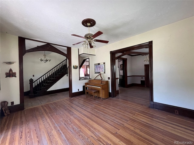 empty room with a textured ceiling, dark hardwood / wood-style floors, and ceiling fan with notable chandelier