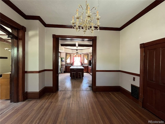 hallway with dark wood-type flooring, ornamental molding, and an inviting chandelier