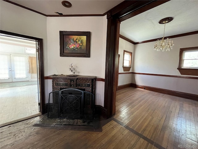 unfurnished living room with an inviting chandelier, ornamental molding, and hardwood / wood-style flooring