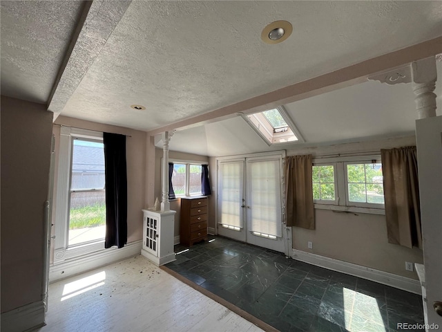 foyer featuring a healthy amount of sunlight, a textured ceiling, french doors, and lofted ceiling with skylight