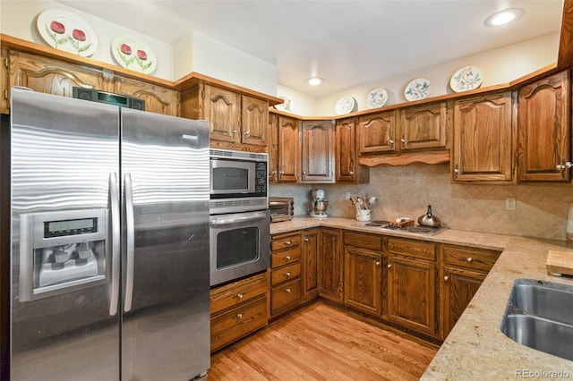 kitchen with sink, stainless steel appliances, light stone countertops, decorative backsplash, and light wood-type flooring