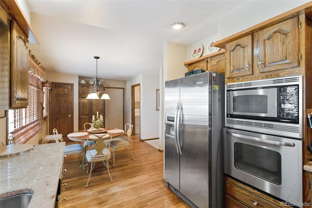 kitchen featuring sink, light stone counters, decorative light fixtures, light wood-type flooring, and appliances with stainless steel finishes