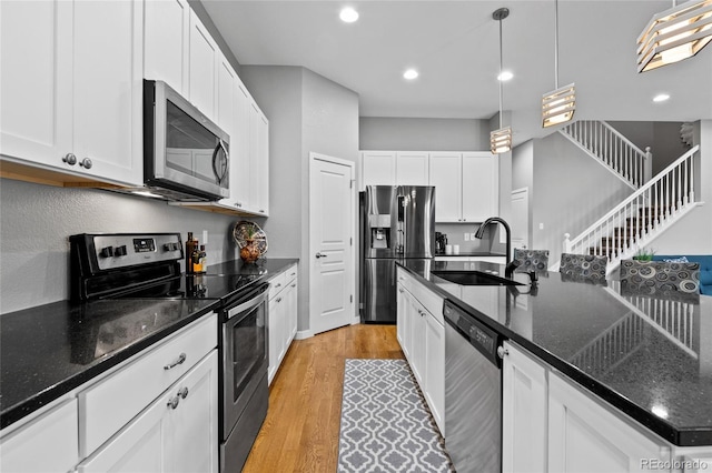 kitchen with light wood finished floors, white cabinets, appliances with stainless steel finishes, hanging light fixtures, and a sink