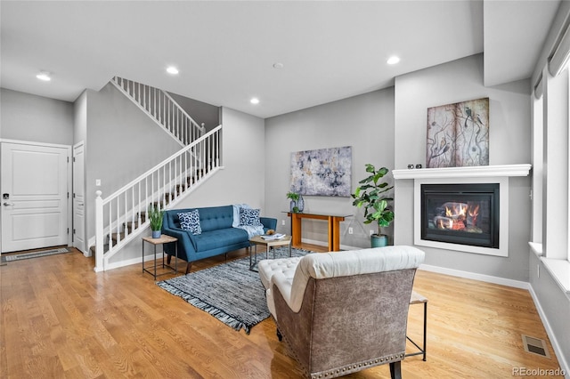 living room with stairs, a glass covered fireplace, wood finished floors, and visible vents