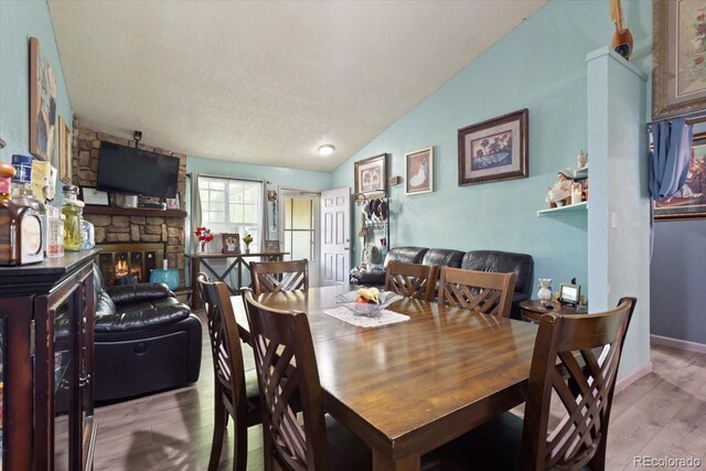 dining space with a stone fireplace, vaulted ceiling, light hardwood / wood-style floors, and a textured ceiling